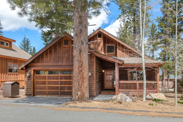 Une cabane en bois rustique, dotée d’un garage, de grandes fenêtres et d’un porche.