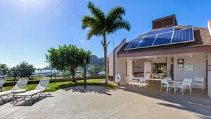 Ein Gebäude mit Solaranlage, Außenbestuhlung und einer Palme.
