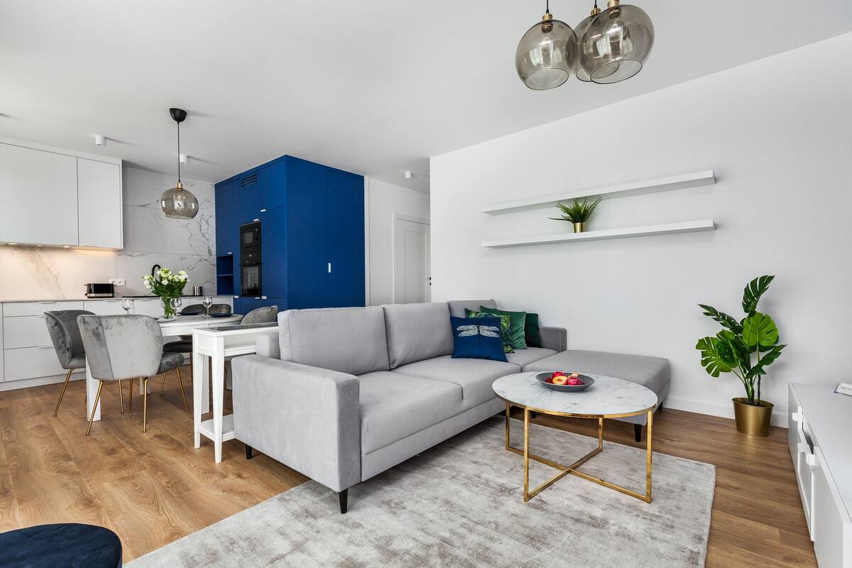 Una sala de estar moderna con un sofá gris, una mesa redonda y una zona de comedor con una mesa y sillas blancas.