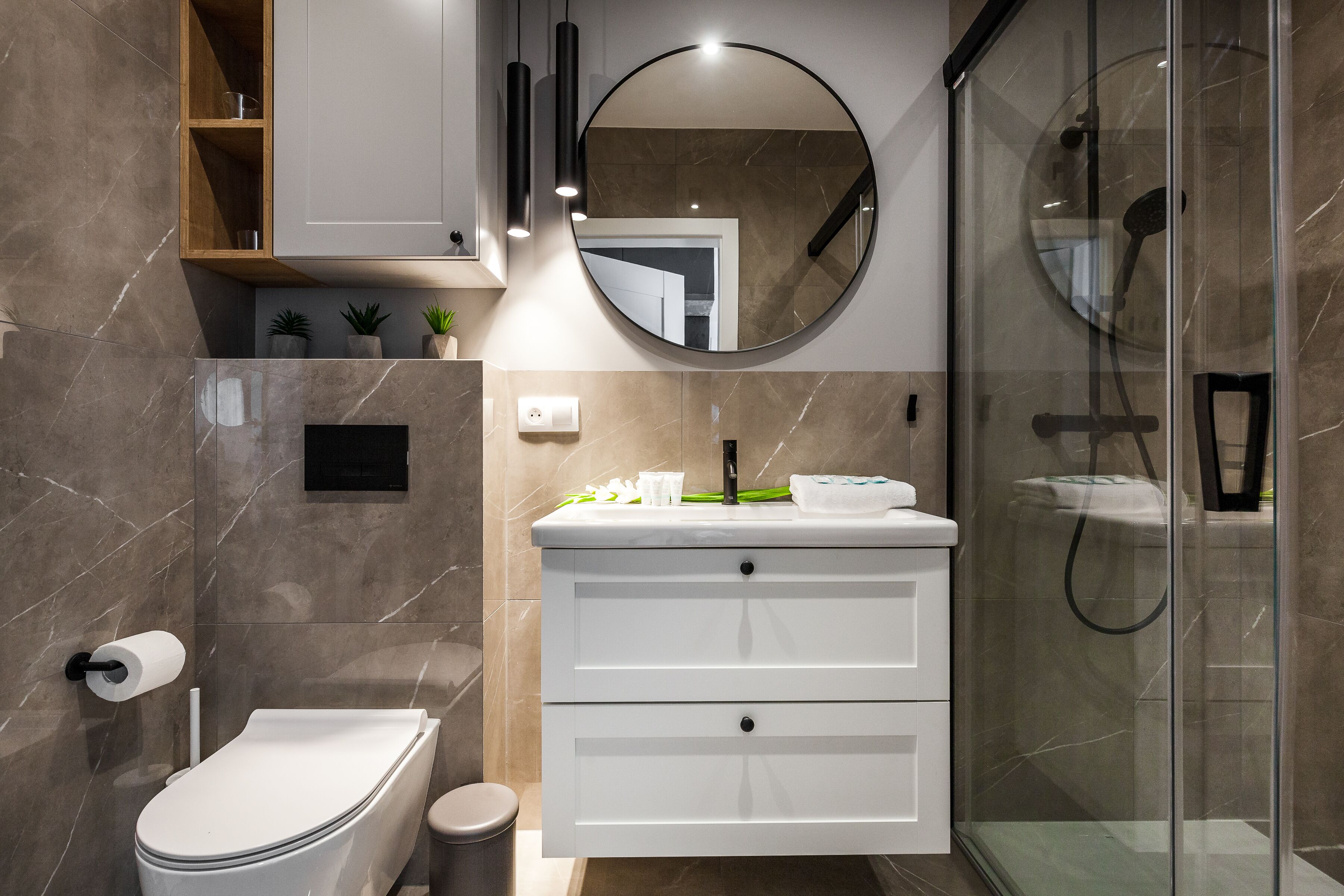 A modern bathroom with a toilet, vanity, and glass shower enclosure.