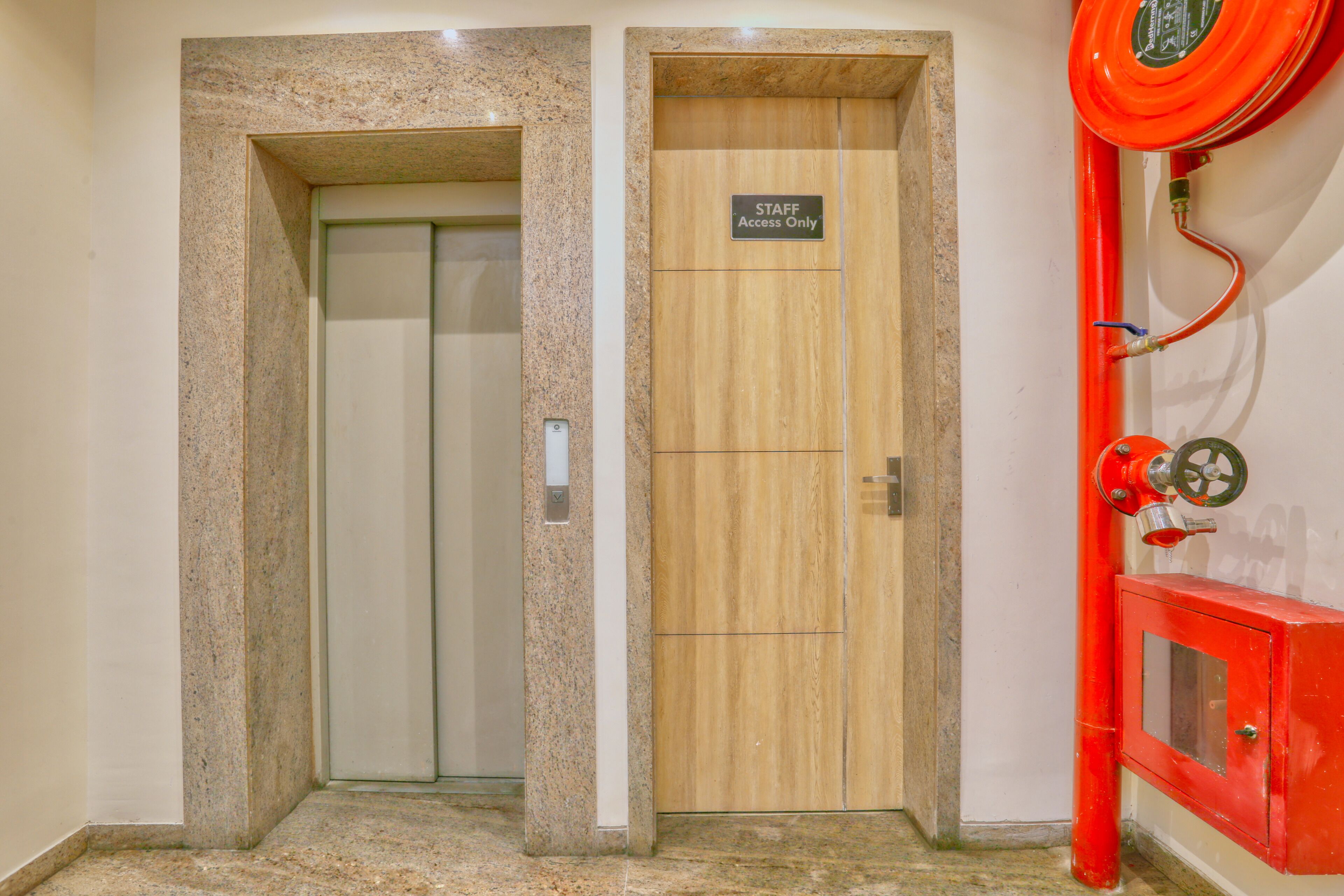 An elevator with a sign indicating it is for staff access only, a red fire extinguisher mounted on the wall, and a marble floor.