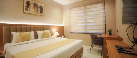 A hotel room with a large bed, a desk, and a chair.