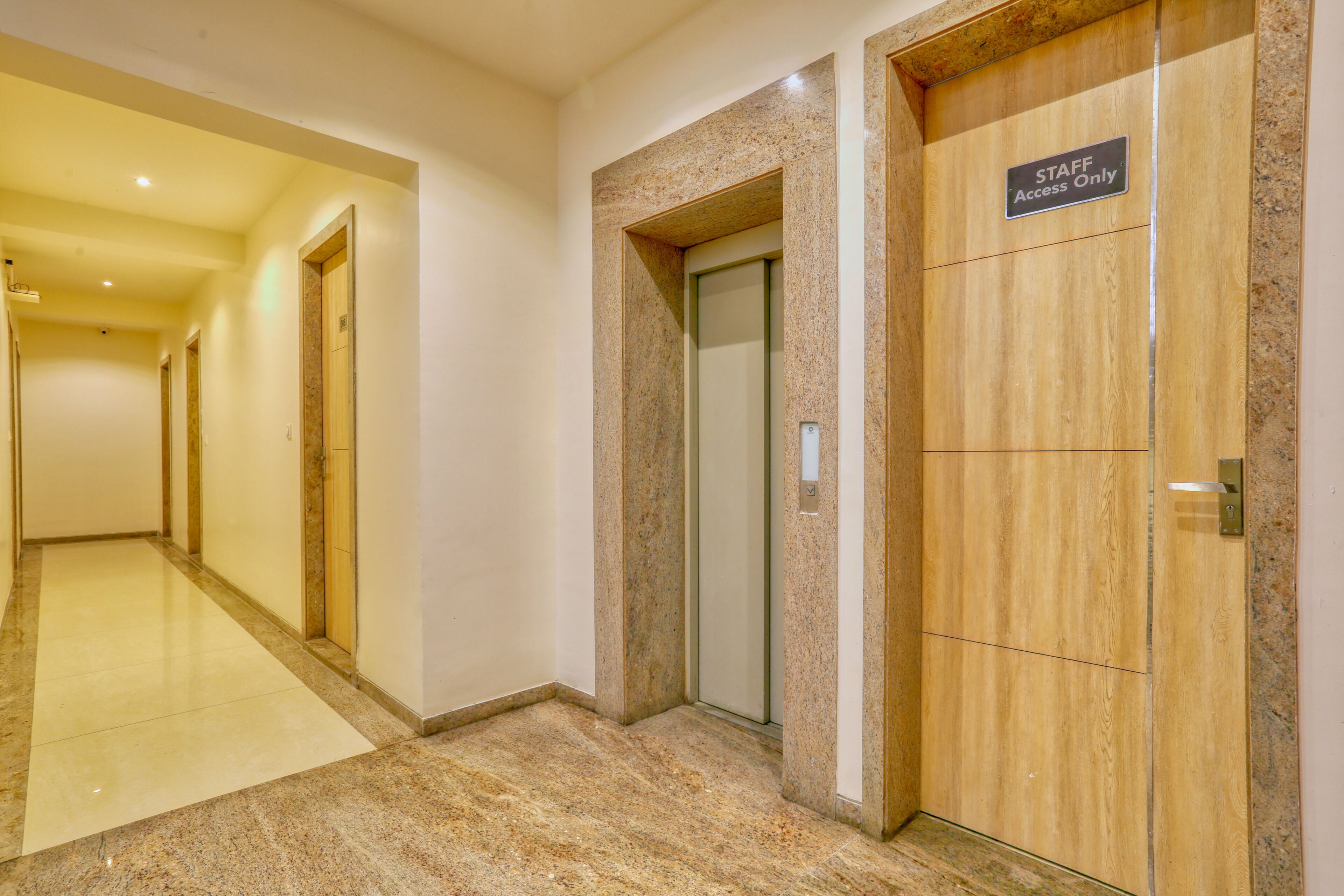 A hallway with a staff-only elevator, a door with a sign, and a marble floor.