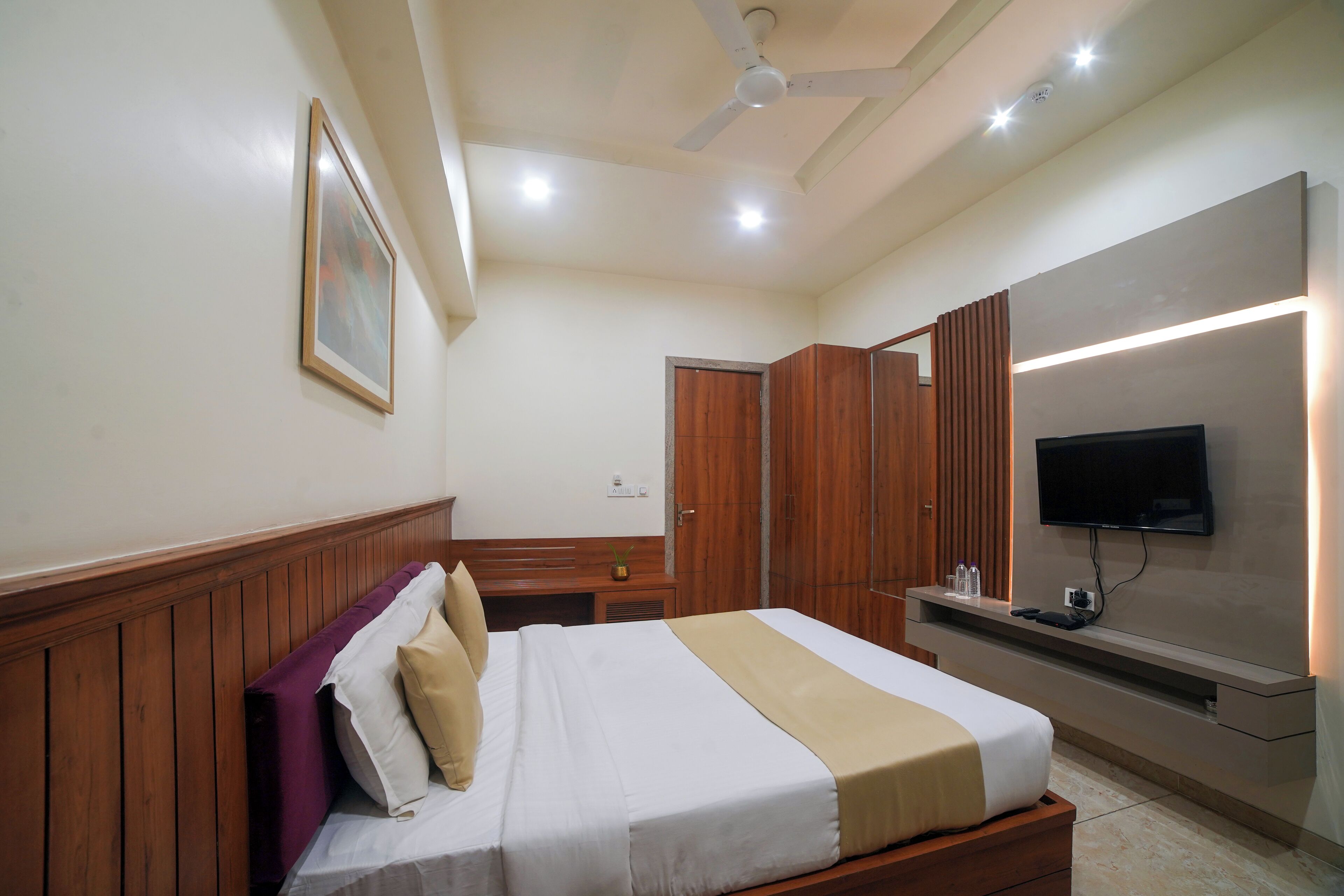 A hotel room with a bed, wooden paneling, a television, and a ceiling fan.