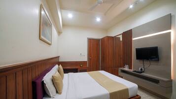 A hotel room with a bed, wooden paneling, a television, and a ceiling fan.