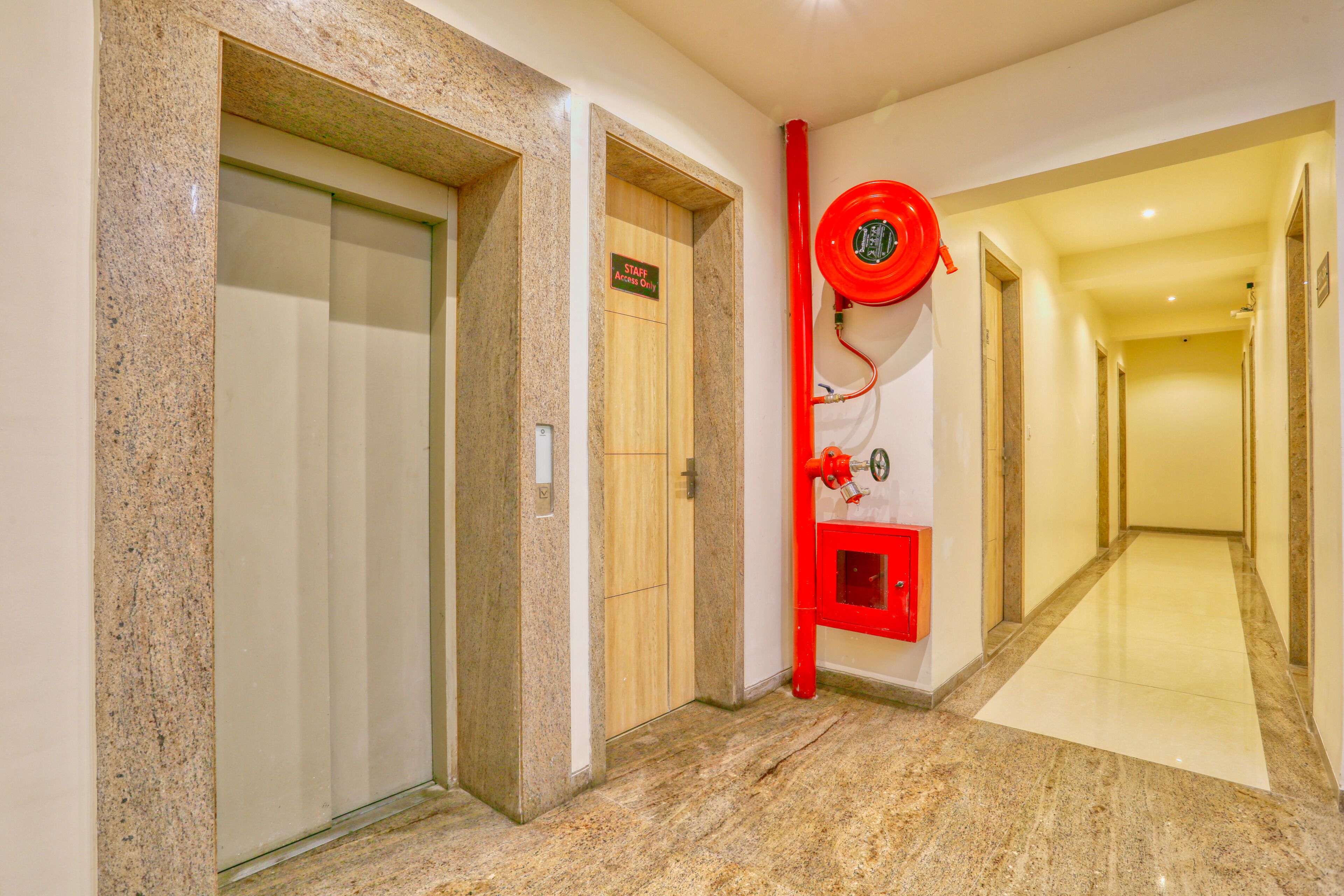 A hotel hallway with a marble floor, a red fire hose, and a door marked "STAFF Only".