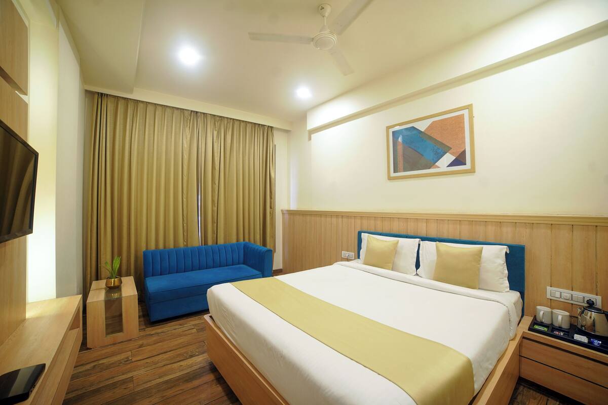 Camera d'albergo con un letto, un divano blu, un comodino in legno, una televisione e una ventola a soffitto.