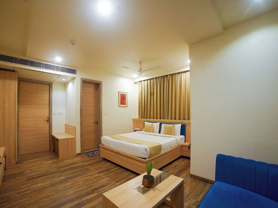 A hotel room with a bed, a desk, a blue sofa, a ceiling fan, and a window with curtains.