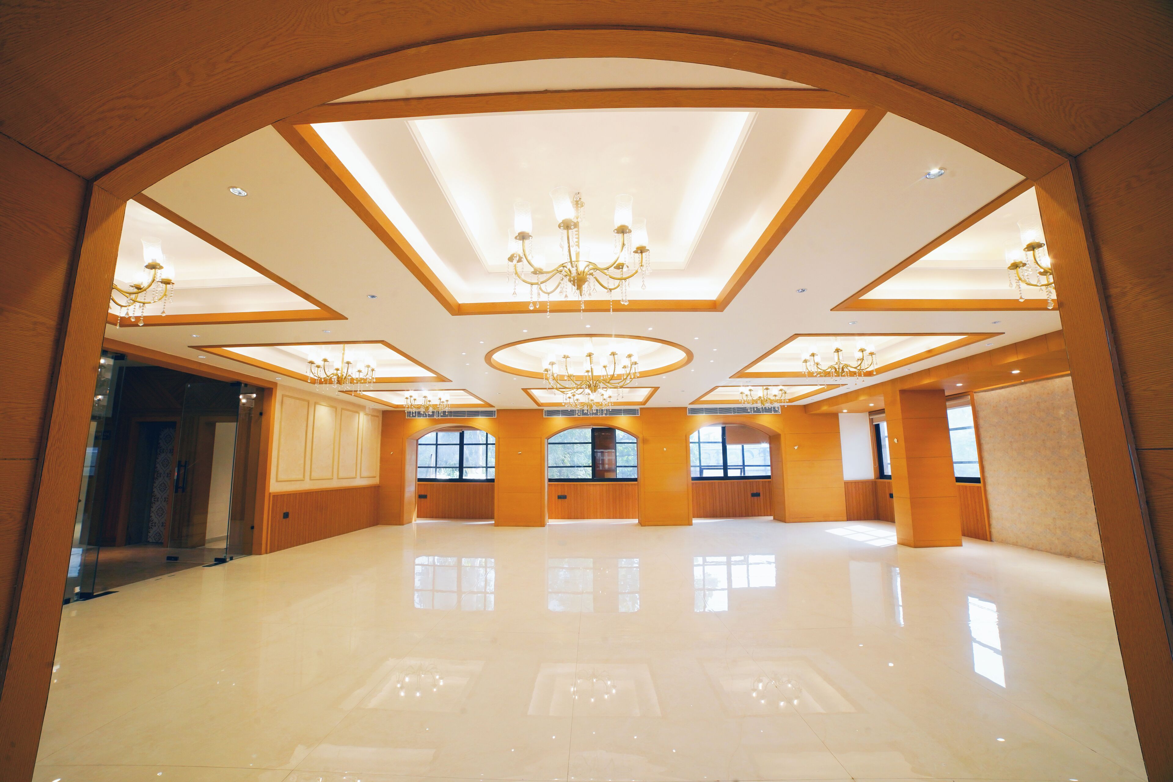 A spacious, well-lit room with a high ceiling, chandeliers, and large windows.