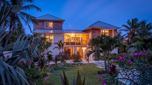 A two-story house with a balcony, surrounded by tropical plants and a well-maintained lawn. - Sea Oats, Hope Town - Luxury Beachfront Home (Hope Town)