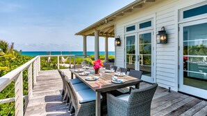A covered outdoor dining area with a view of the ocean, furnished with wicker chairs and a table set for four. - Sea Oats, Hope Town - Luxury Beachfront Home (Hope Town)
