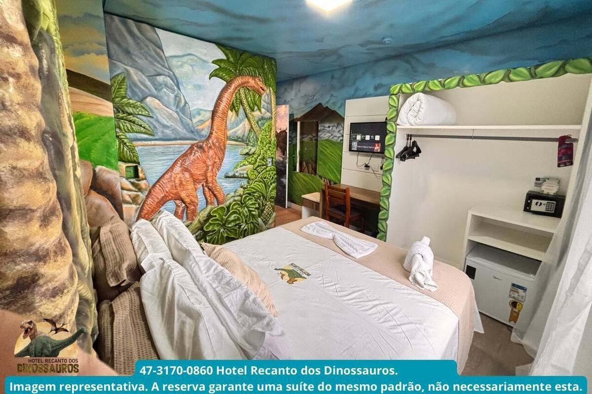 Habitación de hotel temática de dinosaurios, con un mural, una cama, un escritorio y un armario.
