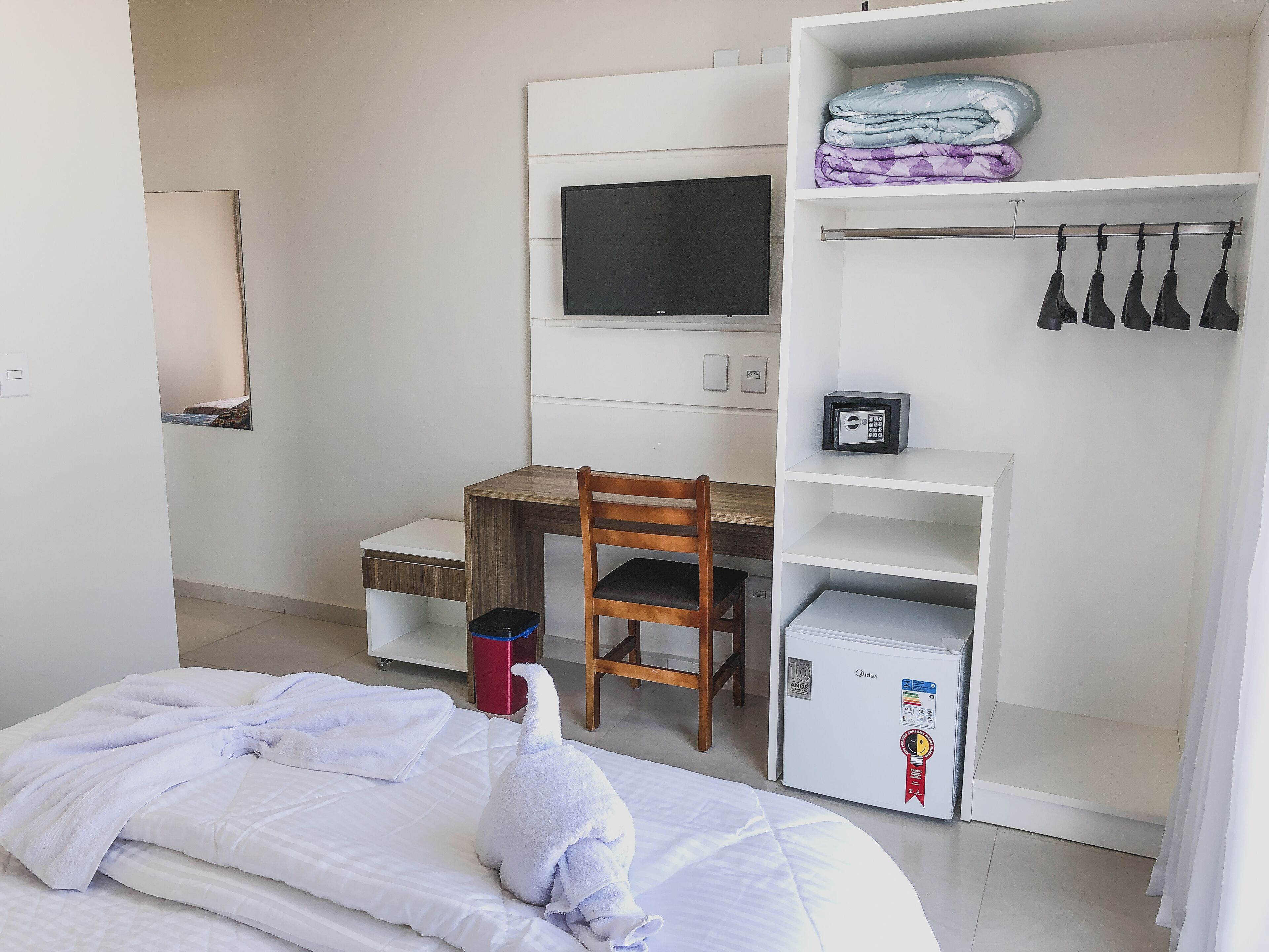 A hotel room with a bed, a desk, a chair, a TV, a wardrobe, and a mini-fridge.