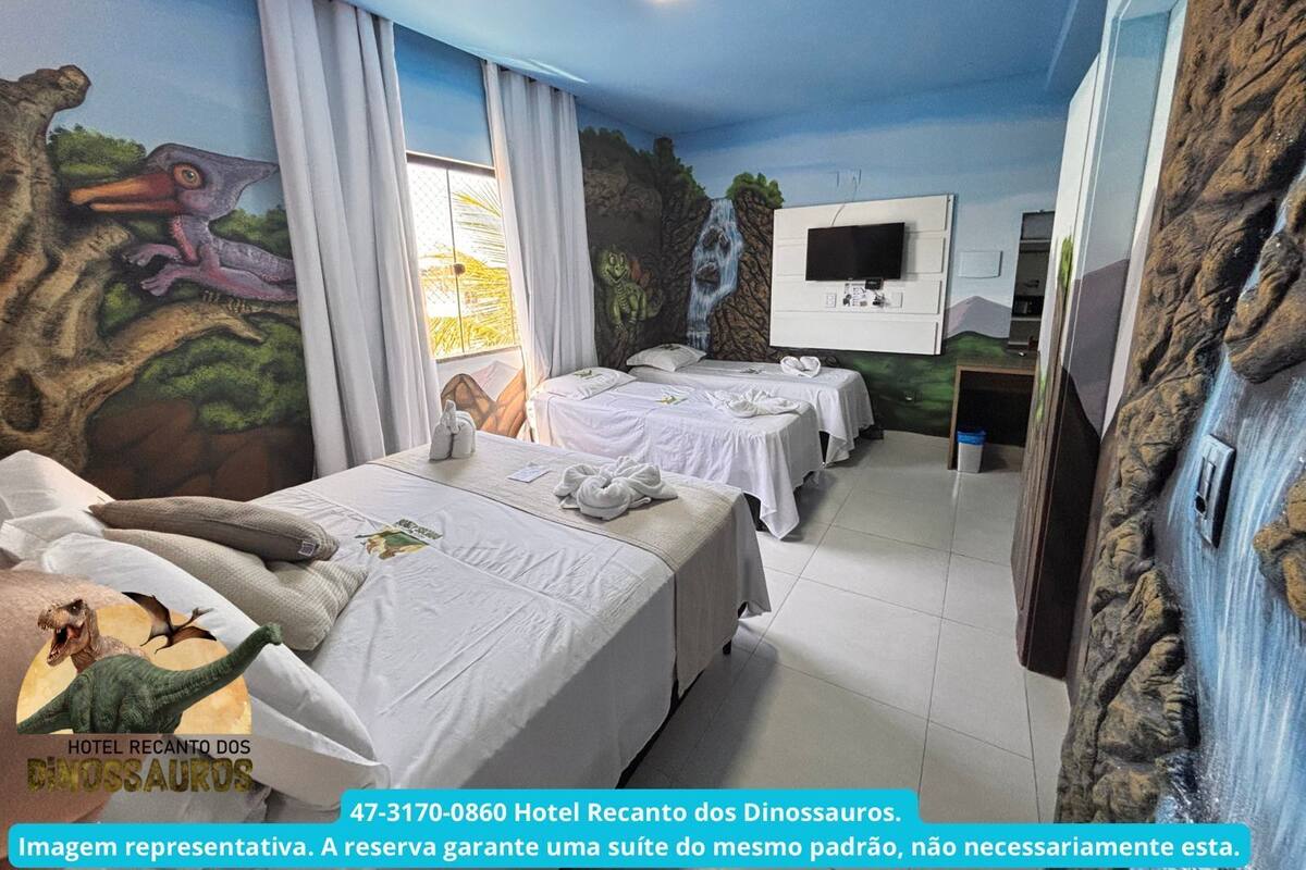 Habitación de hotel con murales de temática de dinosaurios, dos camas, televisor y ventana con cortinas.