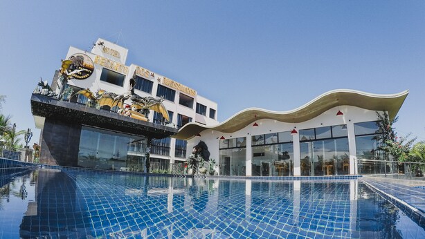 Un hotel con piscina, un edificio grande de techo curvo y una estatua al borde de la piscina.