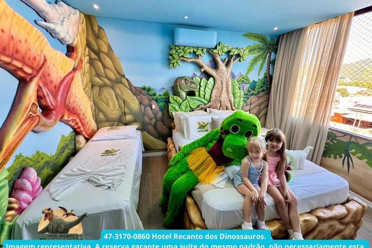 Una habitación con un mural con temática de dinosaurios, una cama y un gran peluche de dinosaurio.