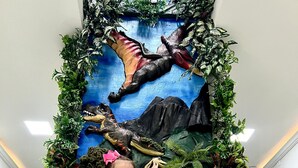 Niño sentado en un banco de mármol frente a un mural con un dinosaurio y plantas.