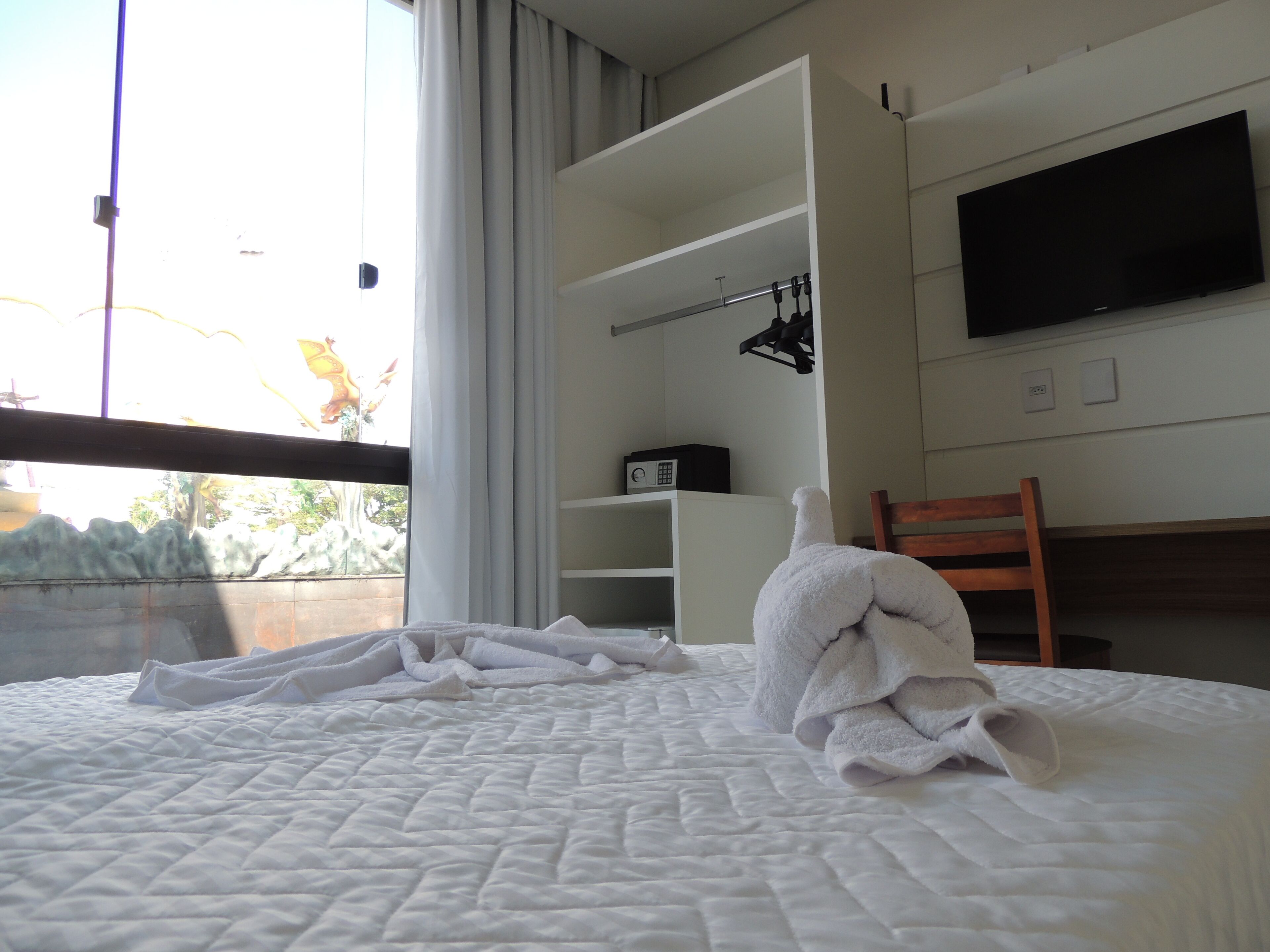 A hotel room with a bed, a television mounted on the wall, and a window with curtains.
