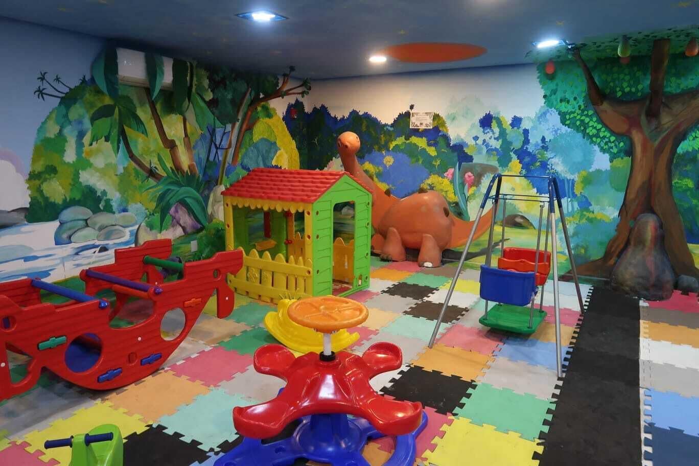 A play area with colorful play structures, a small house, and a mural of a jungle scene.