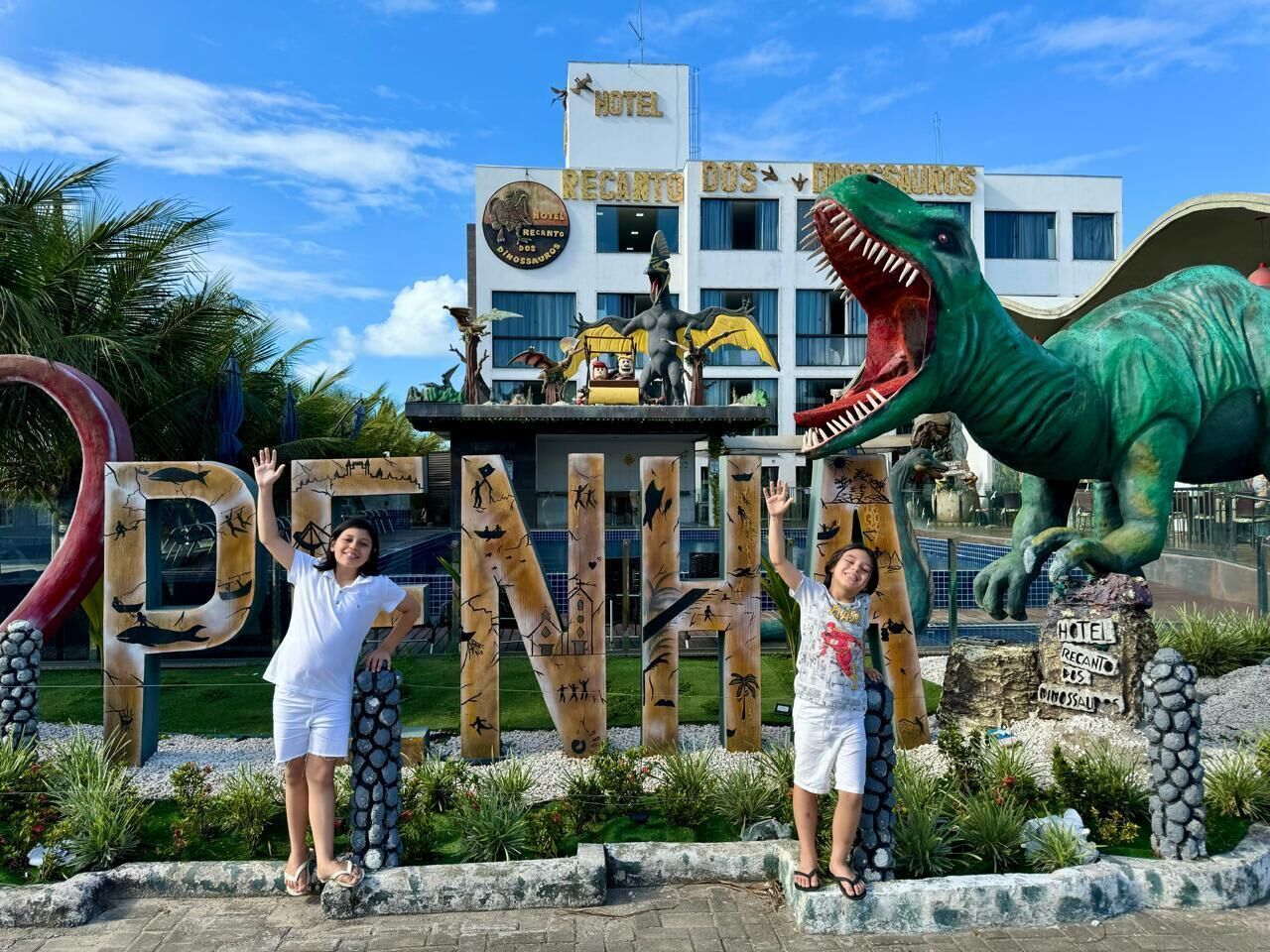 Entrada de un hotel con una estatua de dinosaurio y un gran letrero de madera que dice 'PENINA'.