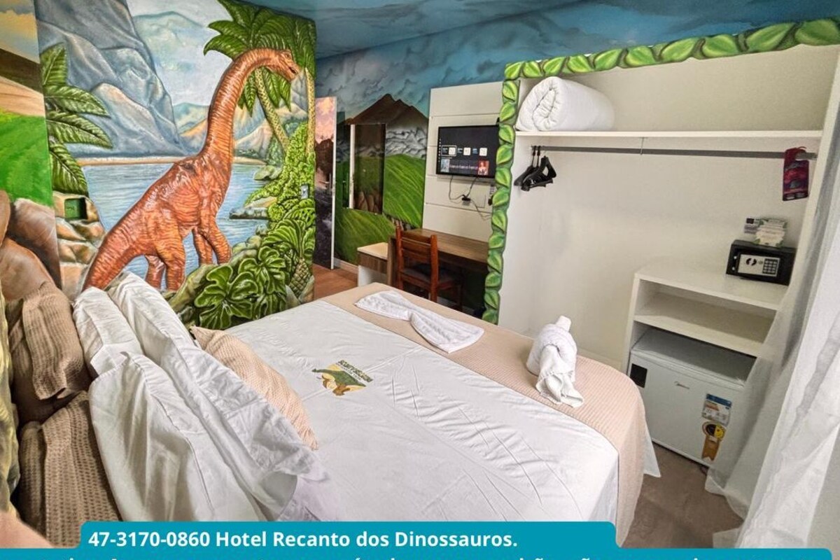Habitación de hotel temática de dinosaurios, con un mural, una cama, un escritorio y un armario.