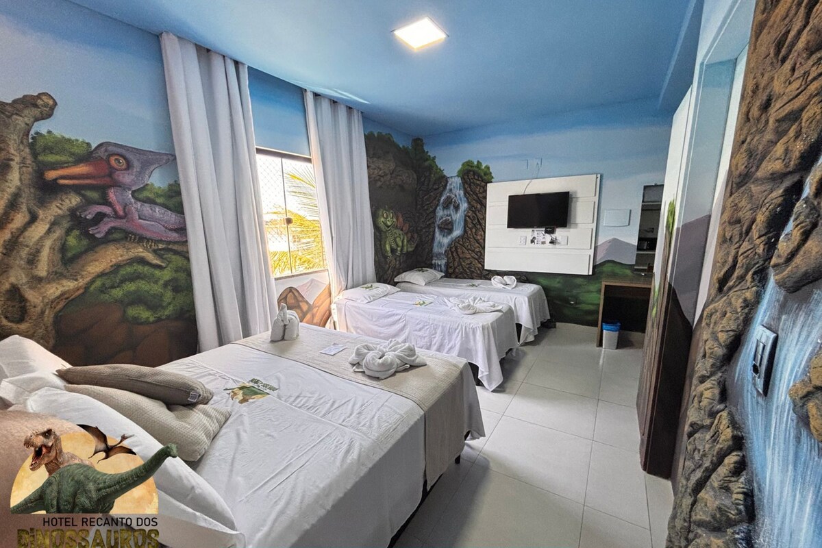 Habitación de hotel con murales de temática de dinosaurios, dos camas, televisor y ventana con cortinas.