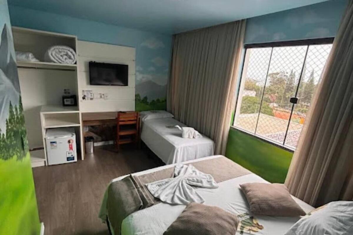 Una habitación de hotel con dos camas, televisión, escritorio y ventana con cortinas.