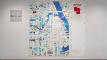 Un mapa colgado en la pared con nombres de calles y un letrero de bienvenida para Oshkosh, WI.