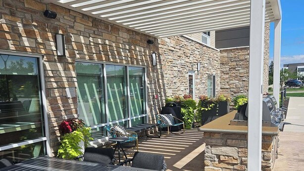 Une terrasse extérieure avec un mur en pierre, un espace salon abrité et un coin barbecue.