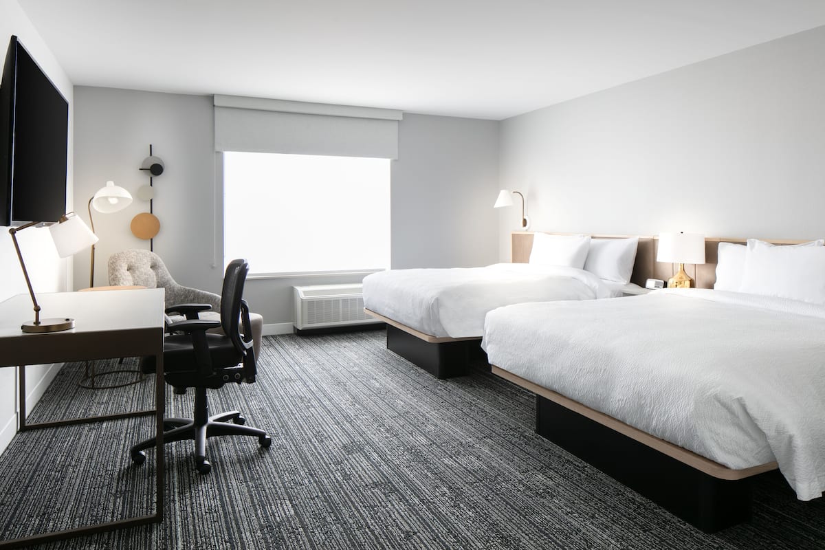 Een hotelkamer met twee bedden, een bureau, een stoel, een televisie en een groot raam.