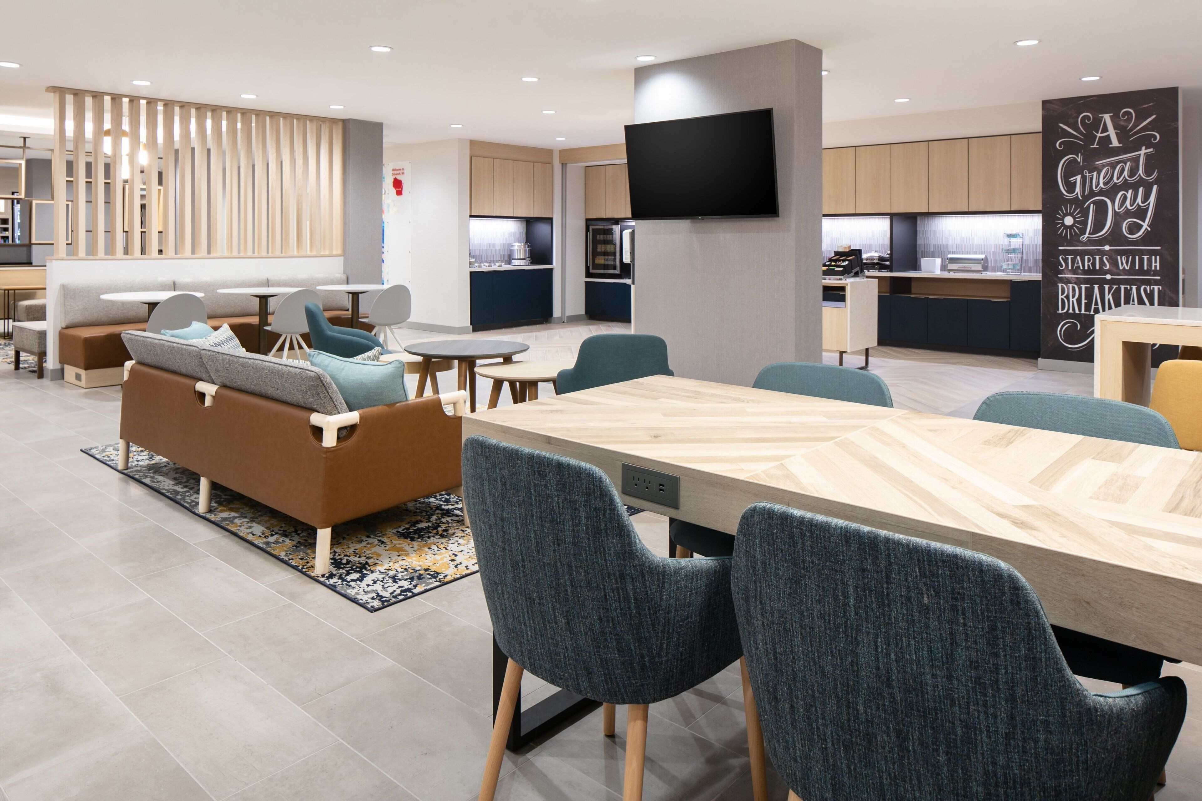 A modern hotel lobby with a dining area, seating arrangements, and a kitchen in the background.