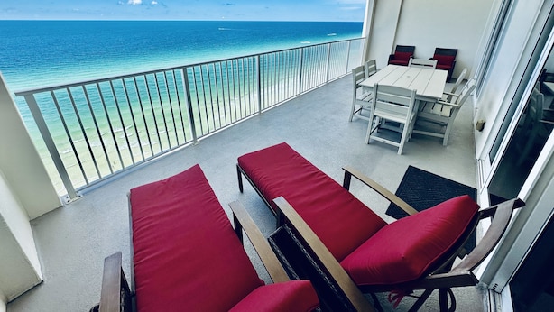 A balcony with a view of the ocean, a table with chairs, and red cushioned chairs. - Beach-Front Condo, 2 Reserved Parking Spaces!, Large Balcony, Fabulous Views! (Panama City Beach)