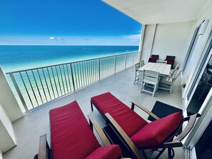 A balcony with a view of the ocean, a table with chairs, and red cushioned chairs. - Beach-Front Condo, 2 Reserved Parking Spaces!, Large Balcony, Fabulous Views! (Panama City Beach)
