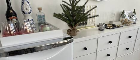Un refrigerador blanco con el nombre de marca 'danny', un mueble blanco con varios cajones y una pequeña planta en maceta encima.