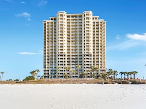 Un hôtel de grande hauteur doté de nombreux balcons, situé sur une plage bordée de palmiers.