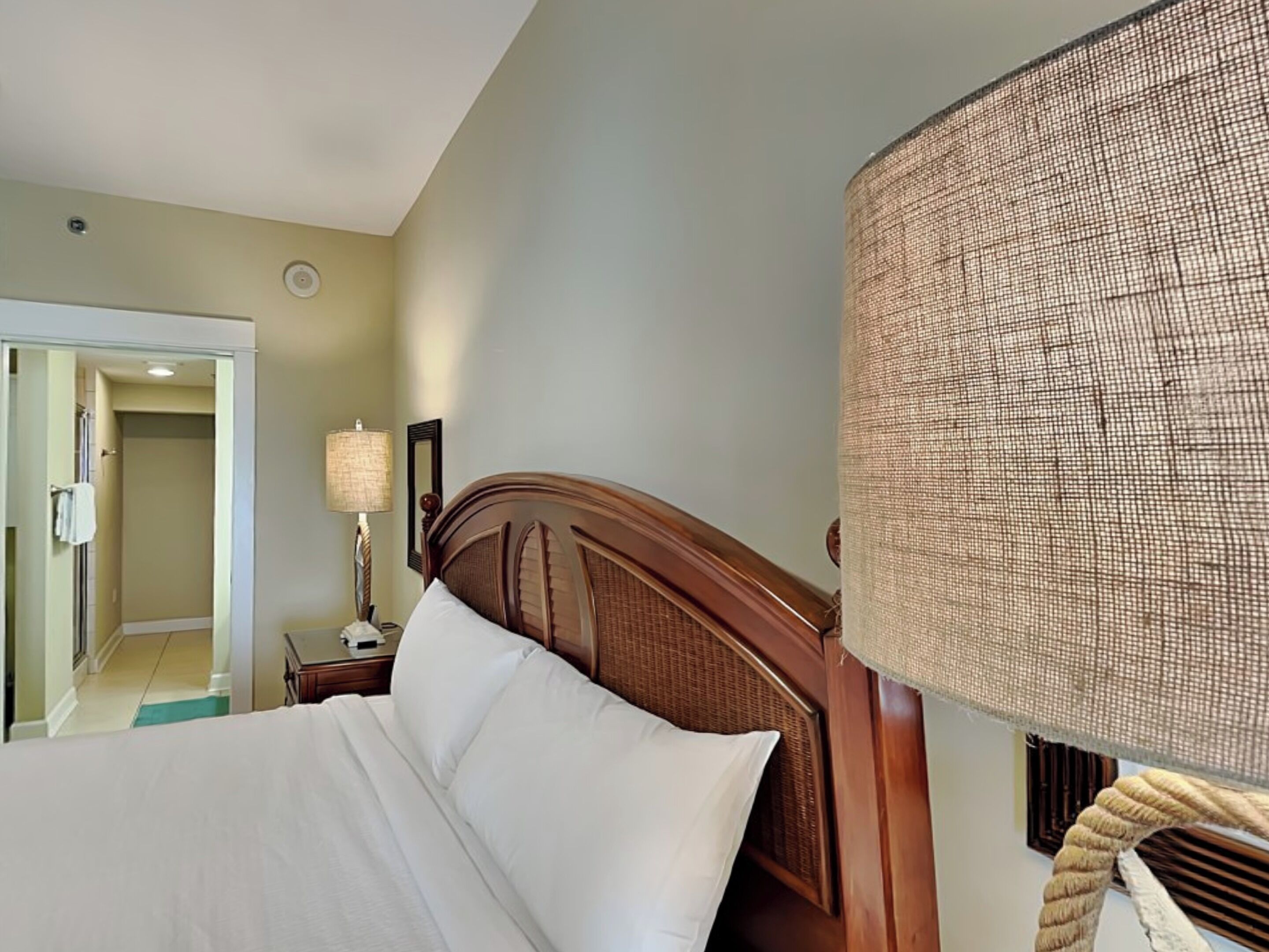 Una habitación de hotel con cabecera de madera, una lámpara grande de fibras tejidas y vistas al pasillo.