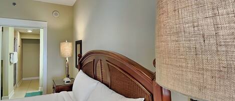 Una habitación de hotel con cabecera de madera, una lámpara grande de fibras tejidas y vistas al pasillo.