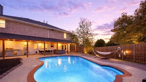 Un giardino con piscina, area barbecue e patio coperto.