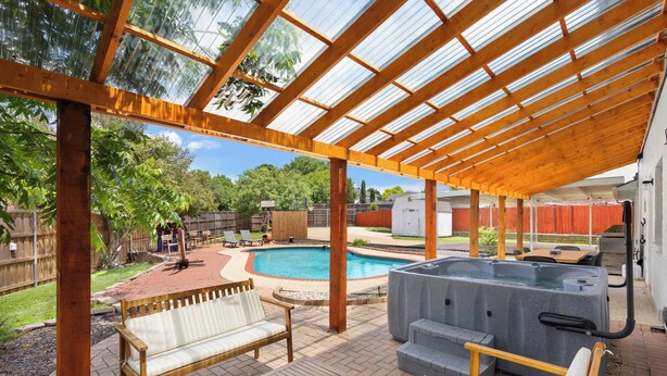 Un’area esterna coperta con una vasca idromassaggio, mobili in legno e una piscina.