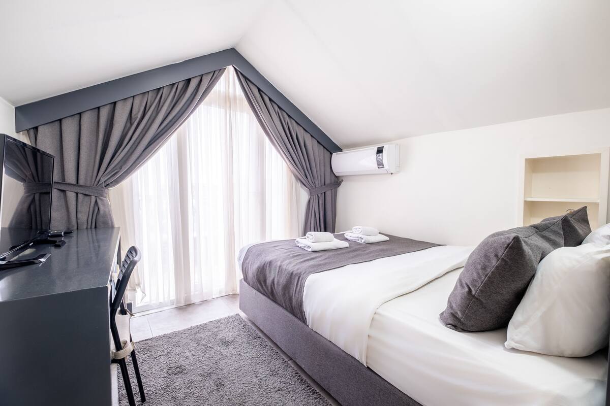 A modern hotel room with a bed, a desk, and a large window with curtains.