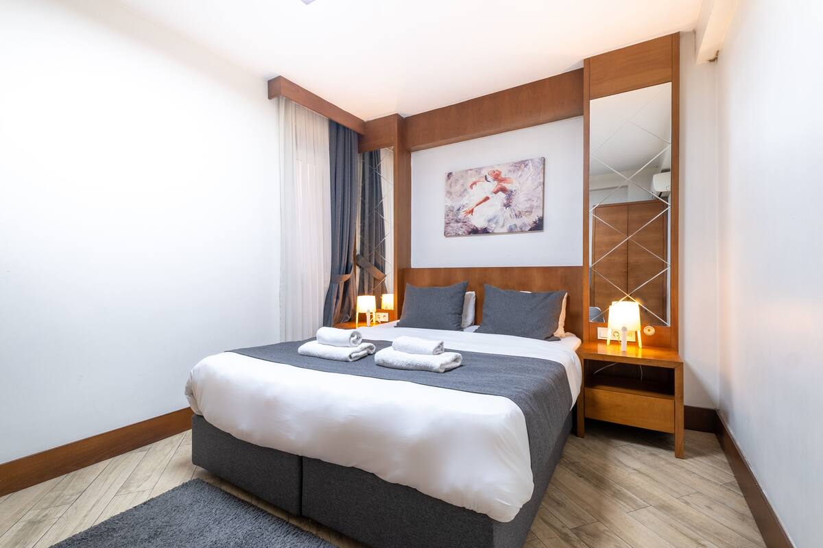 A neatly made bed with a gray and white duvet, a wooden headboard, and a bedside table with a lamp.