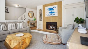 A living room with a grey sofa, a wooden coffee table, a fireplace, and a painting of fish on the wall.