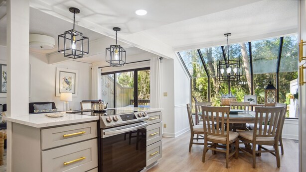 A modern kitchen with a central island, built-in oven, and dining area with wooden chairs and a glass table.