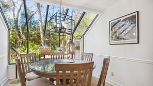 A dining area with a round glass table, wooden chairs, a hanging light fixture, and a framed photograph on the wall.