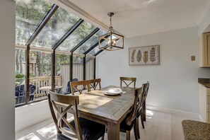 Un comedor con una mesa de madera, sillas, una lámpara colgante y un ventanal con vistas a árboles.