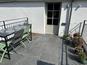 Een terras met een tafel, stoelen, een deur en potplanten.