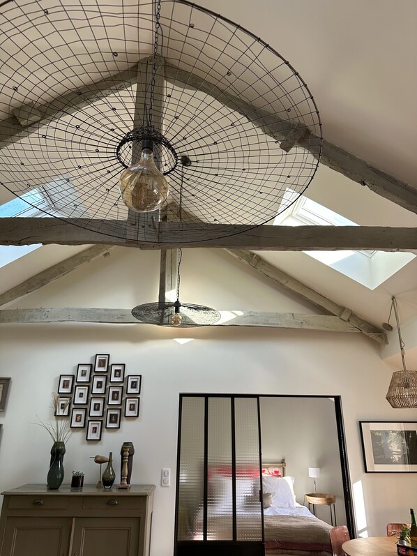 A room with a sloped ceiling, a large fan, a bed, a dresser, and framed pictures on the wall.