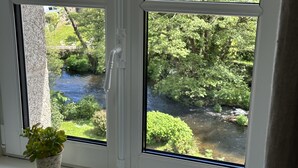 A window with a view of a river and greenery, a potted plant on the windowsill, and a white window frame. - Stylish two bedroom apartment with river views (Pont-Aven)