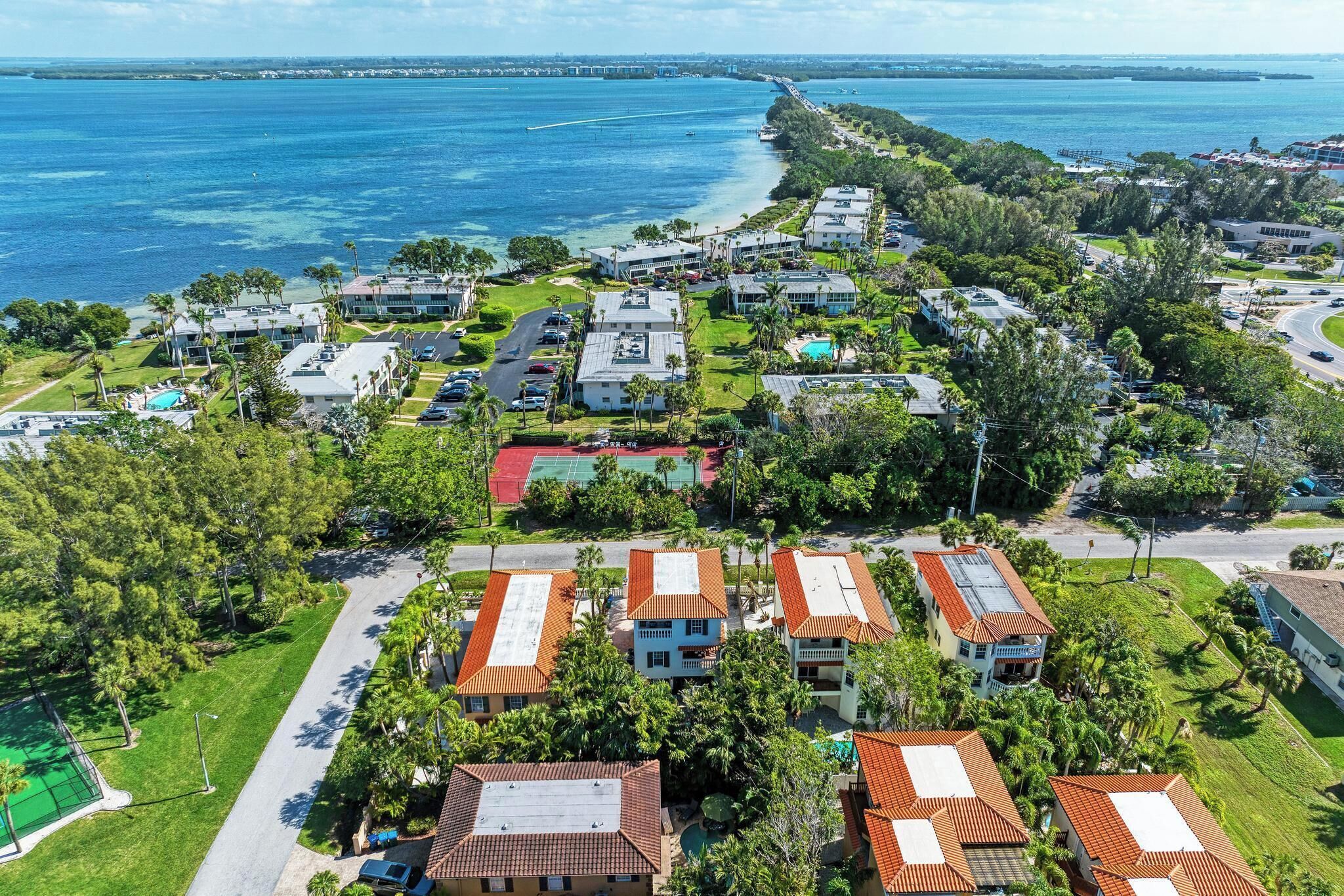 A coastal residential area with houses, a tennis court, and a view of the ocean.