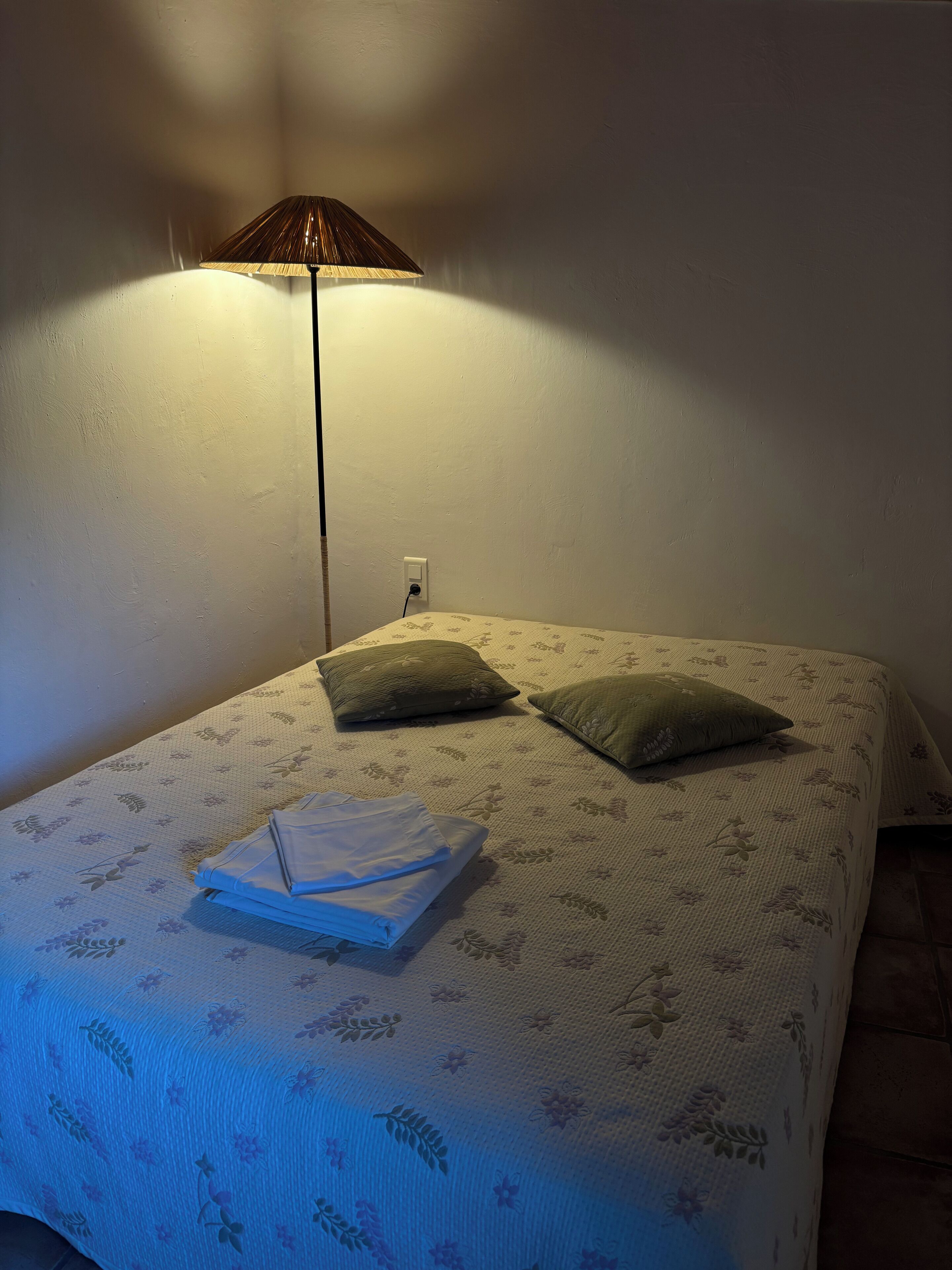 Un lit recouvert d’une couvre-lit à motifs floraux, avec deux oreillers et une serviette blanche pliée.